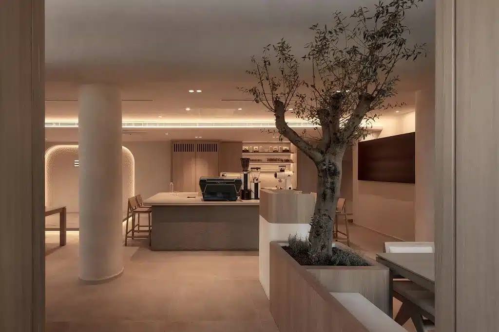 BYD café commercial interior design with central cashier area, pendant lighting, and indoor tree décor creating a modern atmosphere.